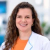 Mujer con cabello rizado y bata blanca sonriendo.
