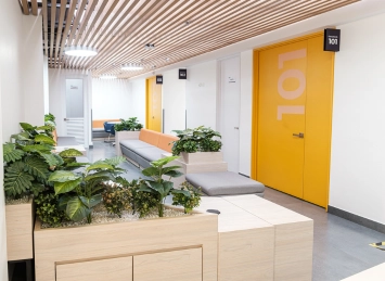Pasillo de la Clínica AVI con bancos y plantas, puerta amarilla número 101